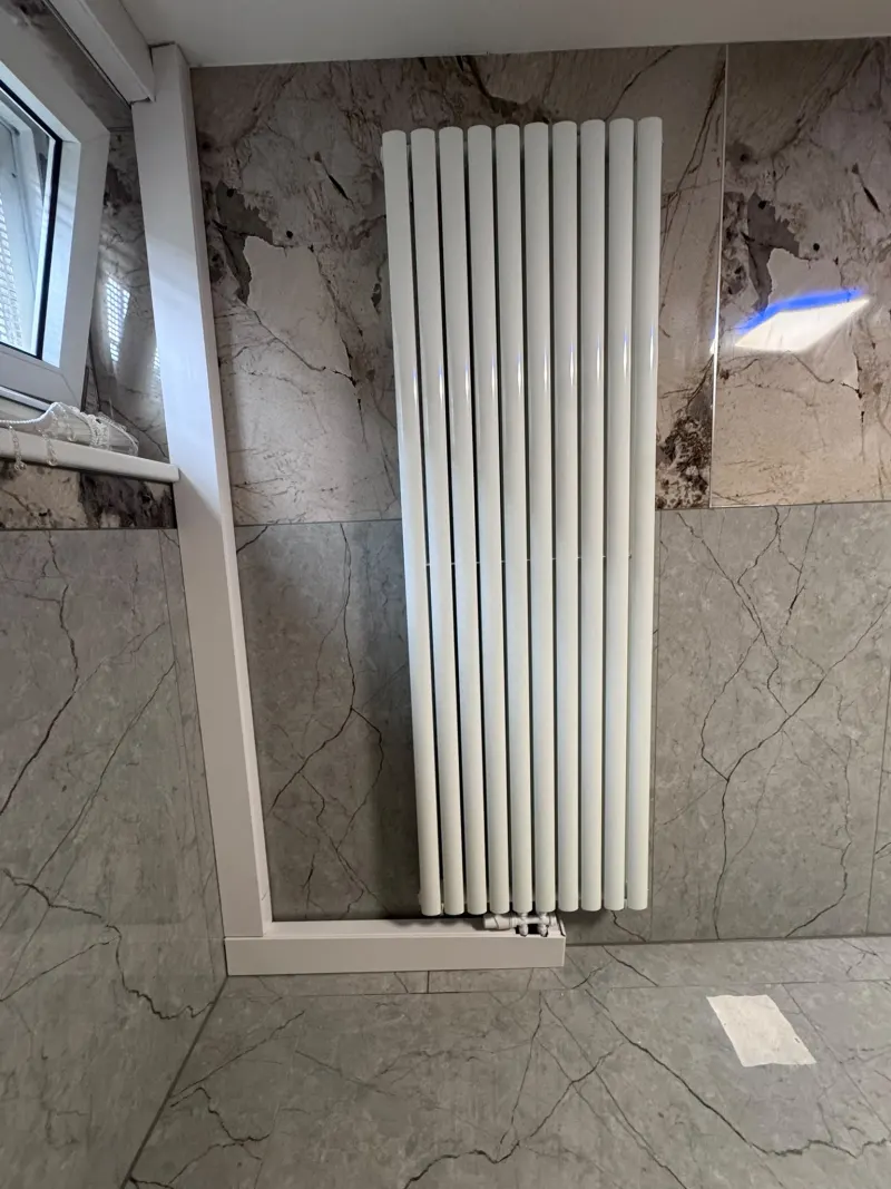 Weißer Röhren-Design-Heizkörper an einer Badwand mit großformatigen Fliesen in Marmoroptik