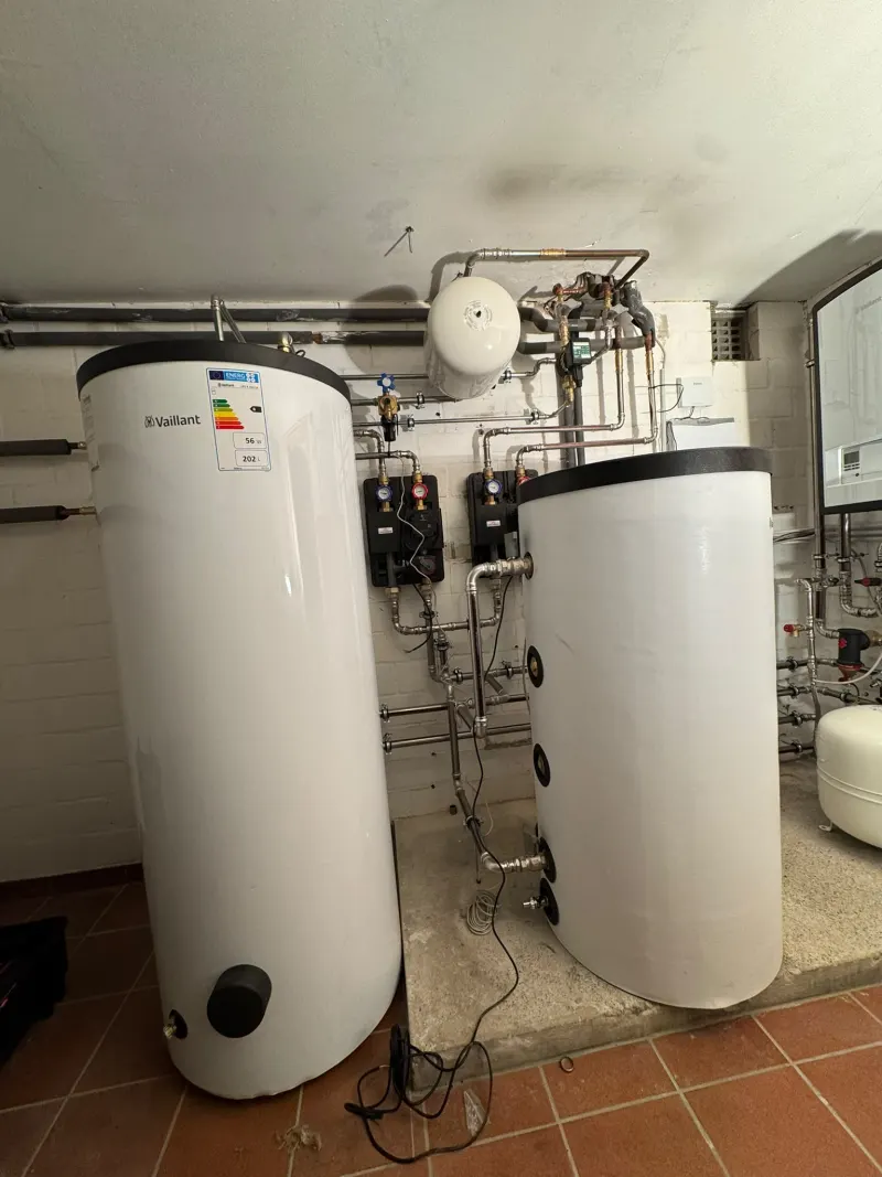 Zwei Speicher im Heizungskeller, dahinter Pumpengruppen und ein Ausdehnungsgefäß an der Wand